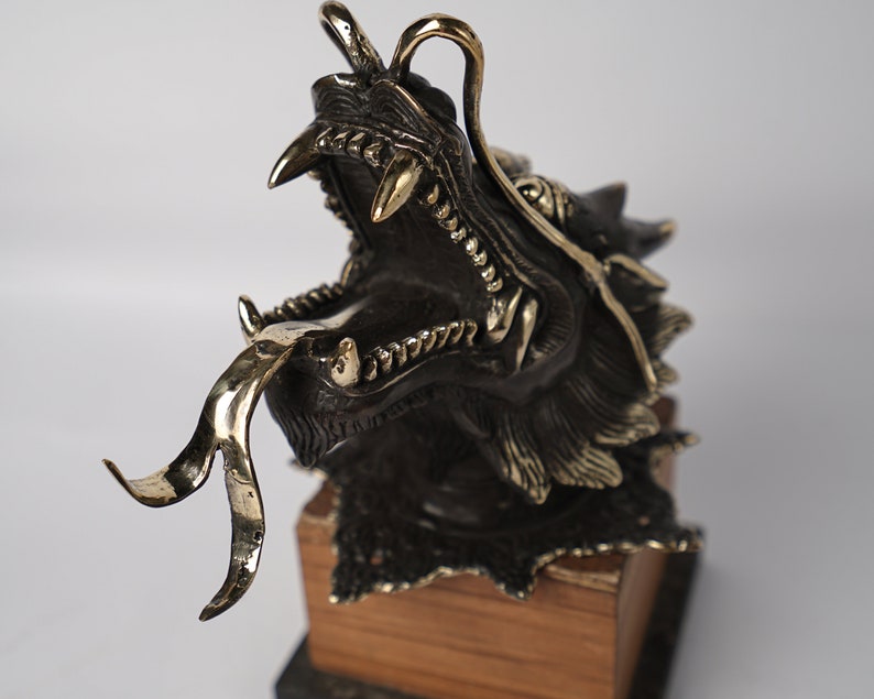 May include: A bronze dragon sculpture with a gold tongue and detailed scales. The dragon is mounted on a wooden base.