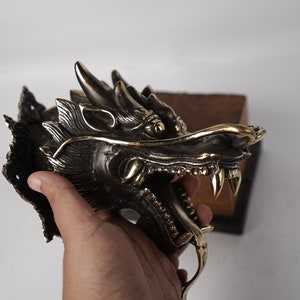 May include: A brass dragon head wall mount with intricate details. The dragon's mouth is open, revealing sharp teeth. The dragon's eyes are inlaid with gold.