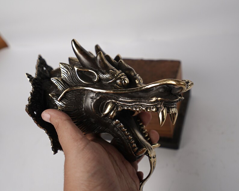May include: A brass dragon head wall mount with intricate details. The dragon's mouth is open, revealing sharp teeth. The dragon's eyes are inlaid with gold.