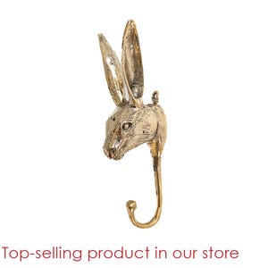 May include: Gold-toned metal rabbit head wall hook. The hook is shaped like a rabbit's head with long ears and a curved hook at the bottom.