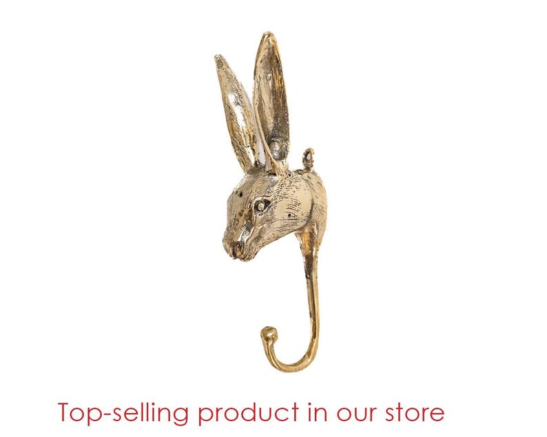 May include: Gold-toned metal rabbit head wall hook. The hook is shaped like a rabbit's head with long ears and a curved hook at the bottom.