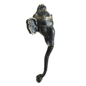 May include: Black metal door handle shaped like the head of the Hindu deity Ganesha. The handle has a gold crown and intricate details.