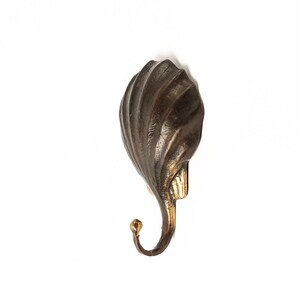 May include: A decorative wall hook made of dark brown metal with a gold-coloured accent. The hook is shaped like a seashell with a swirling design.