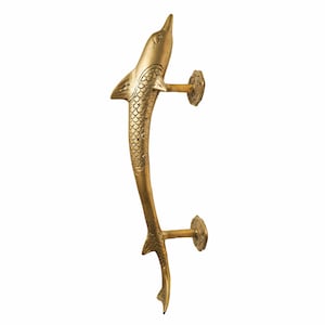 May include: A gold-toned dolphin-shaped door handle with a detailed design. The handle is curved and has a small, round base.