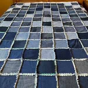 May include: A patchwork quilt made from squares of denim in various shades of blue. The squares are sewn together with a white and light green trim. The quilt is on a bed with a wooden headboard.