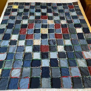 May include: A patchwork quilt made from squares of denim in various shades of blue, with accents of red and white. The quilt is laid out on a white bedspread, showcasing its handmade quality and rustic charm.