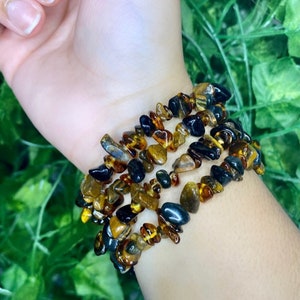May include: A multi-strand bracelet made of small, irregular chips of amber and black gemstone. The bracelet is worn on a person's wrist.