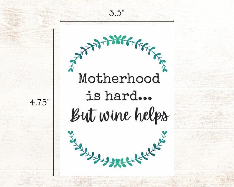 May include: A white card with a green leafy wreath design around the text "Motherhood is hard... But wine helps". The card measures 3.5 inches by 4.75 inches.