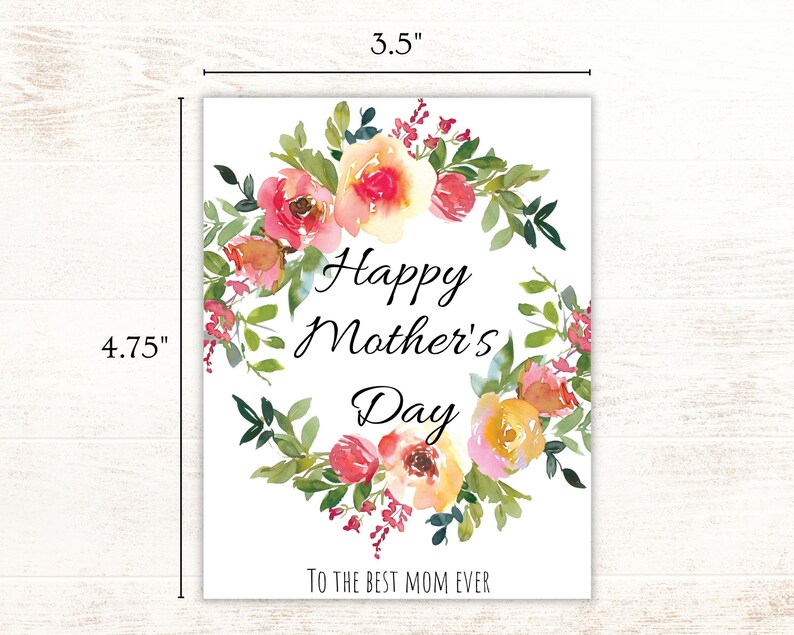 May include: A white card with a floral wreath design in shades of pink, yellow, and green. The text "Happy Mother's Day" is in the center of the wreath, and the text "To the best mom ever" is at the bottom of the card. The card measures 4.75 inches by 3.5 inches.