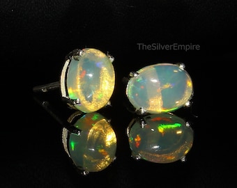 May include: A pair of silver opal earrings with a white opal stone in each earring. The opals have a rainbow iridescent sheen.