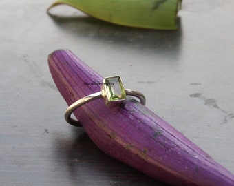 May include: A silver ring with a green gemstone. The ring is resting on a purple surface. TheSilverEmpire is printed on the surface.