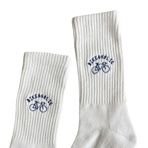 Könnte beinhalten: Ein Paar weiße Socken mit geripptem Schaft und einer dunkelblauen Stickerei, die ein Fahrrad mit dem darüber gebogenen Schriftzug "BIKEHOLIC" zeigt. Die Größe 35-38 ist in Schwarz an der Seite einer Socke nahe dem Fersenbereich aufgedruckt.