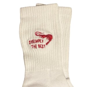 May include: Off-white ribbed crew socks with the text "Shrimply The Best" and a red shrimp graphic. The socks have the size 35-38 printed near the ankle.