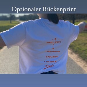 May include: White t-shirt featuring an Aperol Spritz recipe on the back, including Prosecco, Aperol, and soda water. The shirt also has the text "Optionaler R&uuml;ckenprint" at the top.