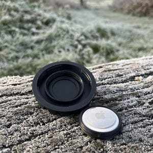May include: A black plastic case with a white lid featuring an Apple logo. The case is open and the lid is lying next to it on a frosty wooden surface.