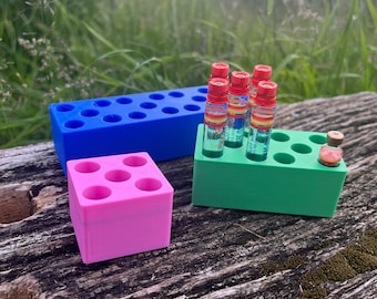 Op de afbeelding: Een set van drie verschillende 3D-geprinte organizers voor kleine items. De blauwe organizer heeft 16 vakjes, de groene organizer heeft 7 vakjes en de roze organizer heeft 6 vakjes. De groene organizer heeft zes kleine glazen flesjes met rode dopjes.