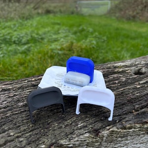 Op de afbeelding: Een verzameling medische benodigdheden, waaronder een blauw en wit plastic apparaat, een witte verpakking en zwarte en witte plastic afdekkingen. Gerangschikt op een verweerd houten oppervlak, met een groene grasachtergrond.