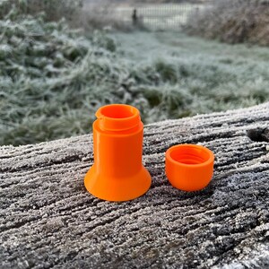 Peut inclure: Un r&eacute;cipient en plastique orange vif avec un couvercle. Le r&eacute;cipient est compos&eacute; de plusieurs pi&egrave;ces qui s'embo&icirc;tent. Le r&eacute;cipient est pos&eacute; sur une surface en bois recouverte de givre.