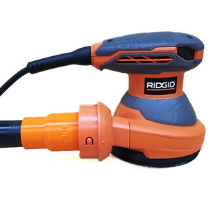 K&ouml;nnte beinhalten: Ein orangefarbener und grauer elektrischer Schleifer mit einem schwarzen Kabel und einem Staubabsauganschluss. Der Schleifer tr&auml;gt den Schriftzug "RIDGID".