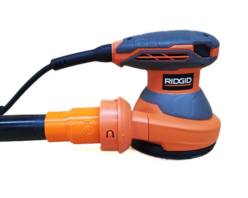 K&ouml;nnte beinhalten: Ein orangefarbener und grauer elektrischer Schleifer mit einem schwarzen Kabel und einem Staubabsauganschluss. Der Schleifer tr&auml;gt den Schriftzug "RIDGID".