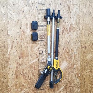 May include: A black and yellow cordless pole saw with a telescopic pole and two batteries. The pole saw is mounted on a wall-mounted storage rack.