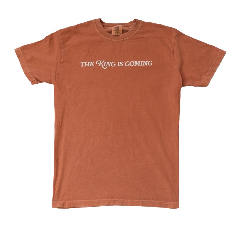 May include: A rust-colored t-shirt with the text "THE KING IS COMING" printed in white on the front.