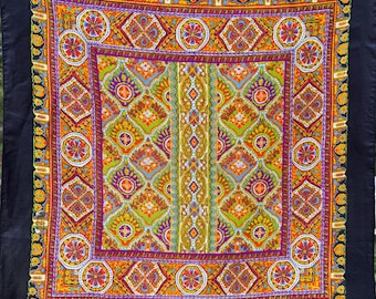Könnte beinhalten: Ein quadratischer Stoff mit schwarzem Rand und einem lebendigen, sich wiederholenden geometrischen Muster. Das Design enthält Orange-, Grün-, Lila- und Blautöne. Der Rand ist mit Blumen- und Paisley-Mustern verziert.