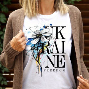 Peut inclure: T-shirt blanc avec un motif noir et blanc d'une fleur et le mot "UKRAINE" avec le mot "FREEDOM" en dessous.
