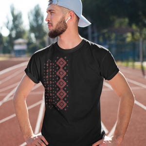 Puede incluir: Camiseta negra con un dise&ntilde;o geom&eacute;trico rojo y blanco en el lado izquierdo. La persona lleva una gorra de b&eacute;isbol azul claro y pantalones deportivos negros. El fondo es una pista de atletismo roja.