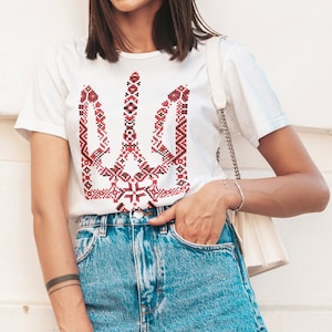 May include: A white t-shirt with a red and black embroidered Ukrainian trident symbol.