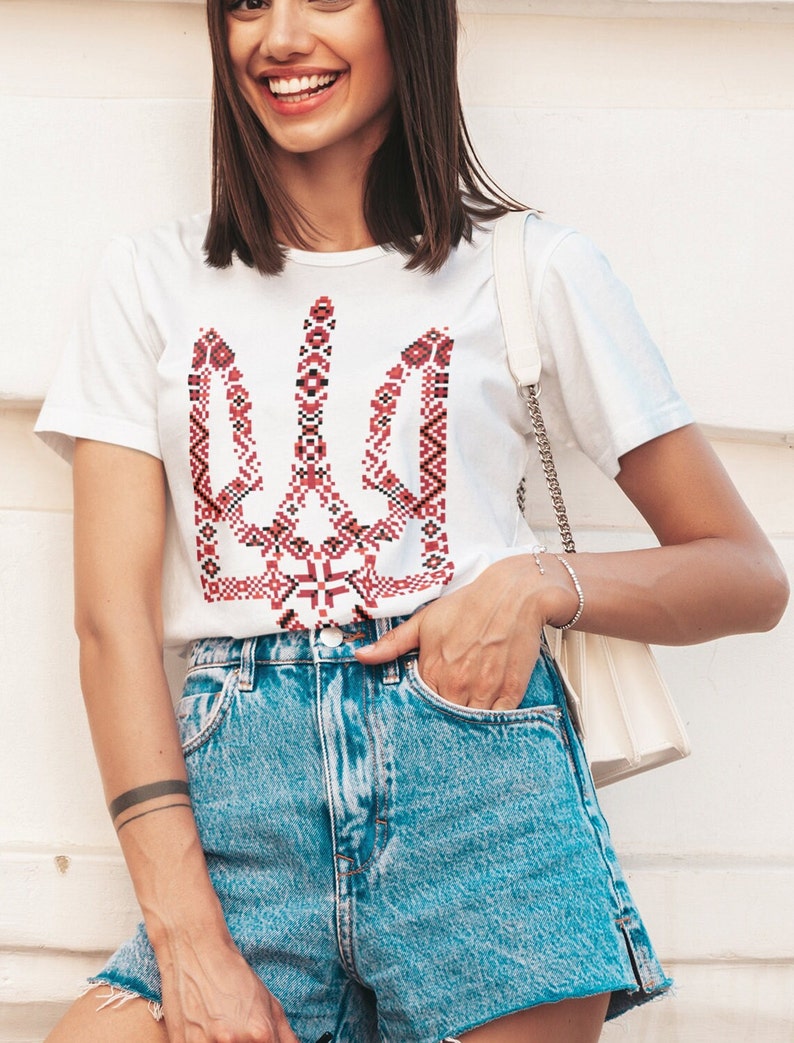May include: A white t-shirt with a red and black embroidered Ukrainian trident symbol.