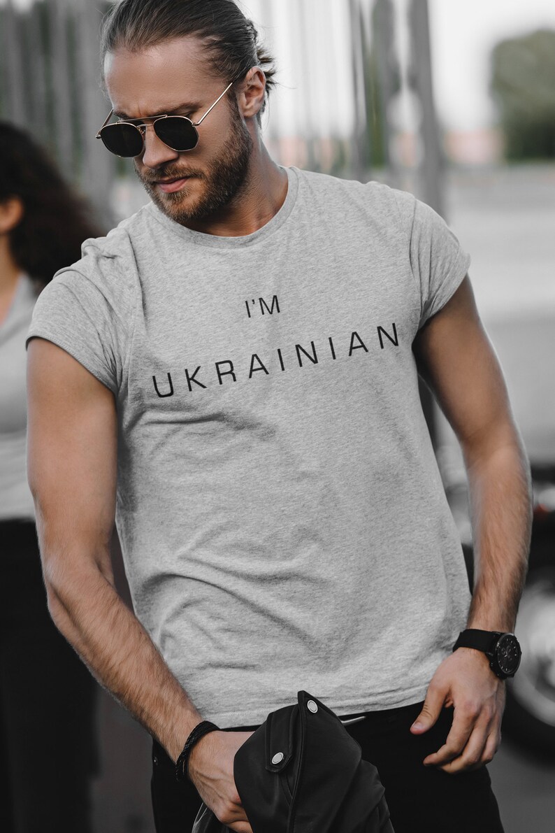 K&ouml;nnte beinhalten: Ein Mann tr&auml;gt ein graues T-Shirt mit dem Aufdruck "I'm Ukrainian". Er tr&auml;gt eine Sonnenbrille und eine schwarze Lederjacke.