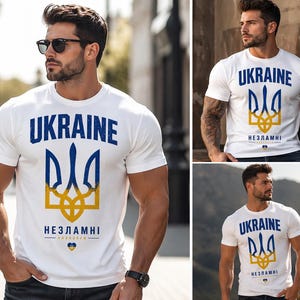 Op de afbeelding: Wit T-shirt met het woord "UKRAINE" in blauw, boven een blauw en geel embleem. De tekst "НЕЗЛАМНІ" staat eronder. Het T-shirt wordt door een persoon gedragen.