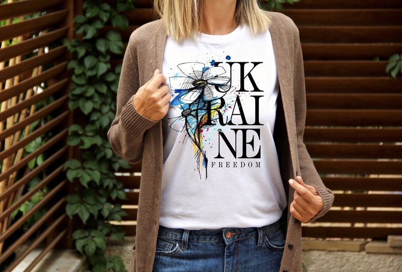 Peut inclure: T-shirt blanc avec un motif noir et blanc d'une fleur et le mot "UKRAINE" avec le mot "FREEDOM" en dessous.