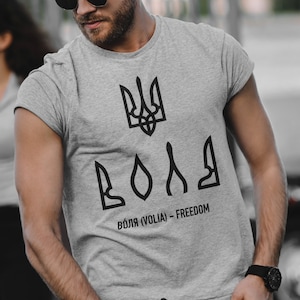 May include: A gray t-shirt with a black Ukrainian trident symbol and the word "ВОЛЯ" (VOLIA) - FREEDOM printed on the front.