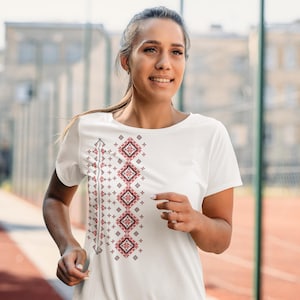 Puede incluir: Camiseta blanca con un dise&ntilde;o bordado geom&eacute;trico en rojo y negro. El dise&ntilde;o est&aacute; alineado verticalmente en el lado izquierdo de la camiseta. La camiseta tiene mangas cortas y cuello redondo.