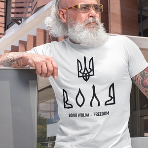 May include: White t-shirt with a black Ukrainian trident symbol and the word "ВОЛЯ" (VOLIA) - FREEDOM printed on it.