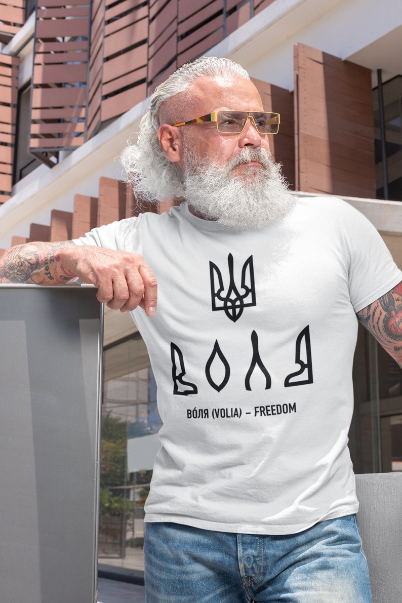 May include: White t-shirt with a black Ukrainian trident symbol and the word "ВОЛЯ" (VOLIA) - FREEDOM printed on it.