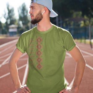 Puede incluir: Camiseta verde oliva con un patr&oacute;n geom&eacute;trico en rojo y gris. La camiseta se usa con pantalones deportivos negros y una gorra de b&eacute;isbol azul claro. La persona est&aacute; de pie en una pista roja.