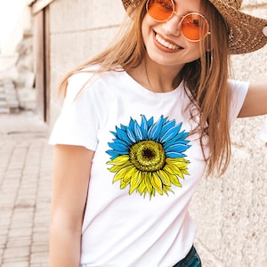 May include: A white t-shirt with a sunflower graphic. The sunflower is yellow and has blue petals. The sunflower is split in half, with the top half being blue and the bottom half being yellow.