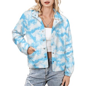 May include: A long-sleeve jacket featuring a sky blue and white cloud print pattern. The jacket has a stand-up collar, a front button closure with silver-toned snaps, and two side pockets. It is worn over a plain white top and blue jeans.