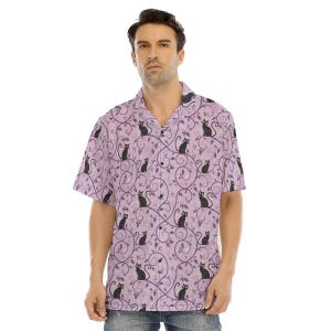 May include: A short-sleeved button-down shirt in a light lavender color featuring a repeating pattern of black cats sitting among dark purple swirling vine and leaf motifs. The shirt has a notched collar and a front button placket closure.