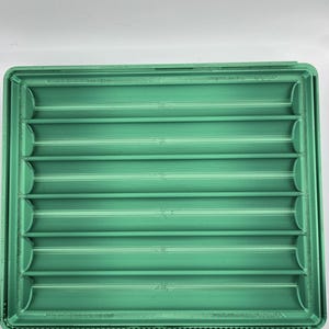 May include: A rectangular green tray featuring six parallel, horizontal, concave channels. The tray has a raised border and a smooth, uniform finish across its entire surface, with visible horizontal lines from the manufacturing process.