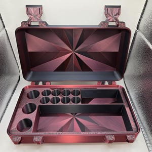 May include: A rectangular storage case with a hinged lid, featuring a deep red and black geometric starburst pattern. The interior contains multiple circular compartments and two rectangular storage sections, all finished in a matte black and red.