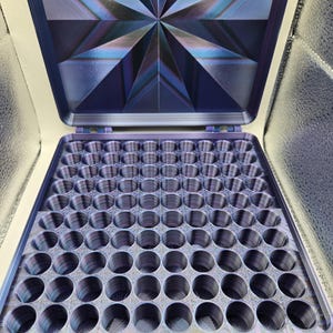 May include: A square storage case with an open lid featuring a dark blue and purple iridescent starburst pattern. The interior base contains a grid of one hundred circular compartments, all finished in a matching dark blue and purple gradient.