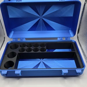 May include: A bright blue rectangular storage case with a hinged lid and black plastic latches. The interior features a black foam insert with eight circular cutouts on the left side and two rectangular compartments for organized storage.