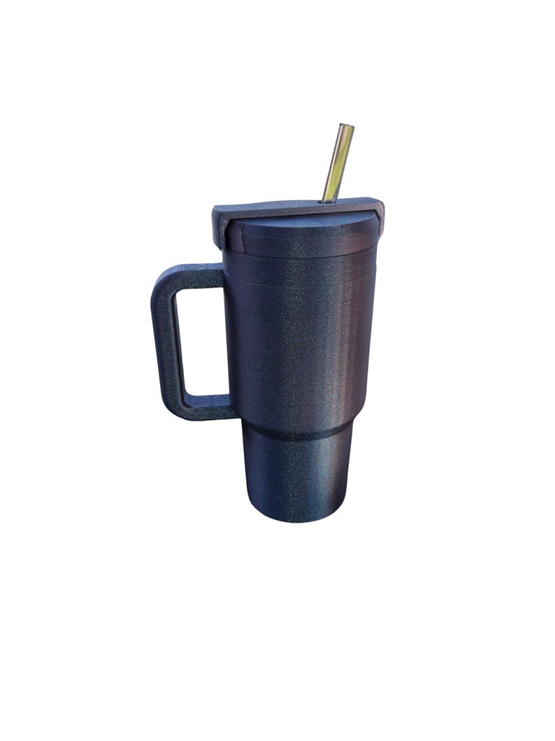 May include: A dark charcoal gray tumbler with a textured, glittery finish, featuring a sturdy side handle, a matching lid, and a straight metallic straw inserted through the top opening. The vessel has a tapered base and a cylindrical body.