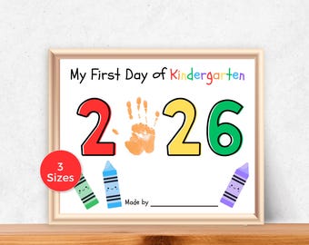 May include: A framed sign featuring the text My First Day of Kindergarten with the year 2026, where the zero is replaced by an orange handprint. The design includes three cartoon crayons in green, blue, and purple, and a red circle stating 3 Sizes.