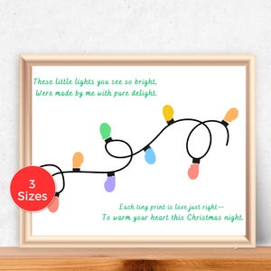 May include: A framed print with a light beige border. The print features a string of colourful Christmas lights with the text "These little lights you see so bright, Were made by me with pure delight." and "Each tiny print is love just right- To warm your heart this Christmas night."