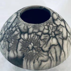 May include: A ceramic vase with a wide, rounded shape and a dark interior. The exterior features a unique pattern of gray and black veining, creating a textured, organic appearance. The vase is a decorative item.